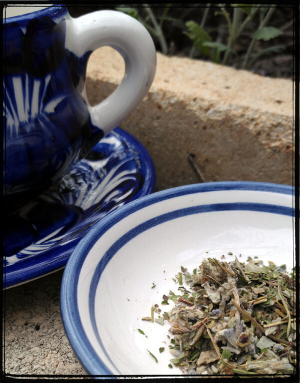 A blue and white ceramic teapot next to a nearly-matching saucer, which holds perhaps a teaspoonful of herbs.