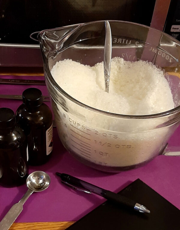 A clear glass measuring bowl filled with white bath salts.