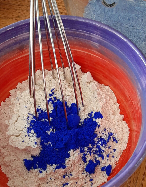 A small pottery bowl with white bath salts, topped with intensely blue powder.