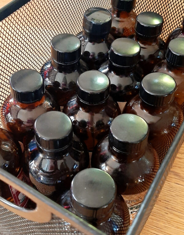 Several amber glass bottles sit in a metal mesh box, just wide enough to hold three bottles across.