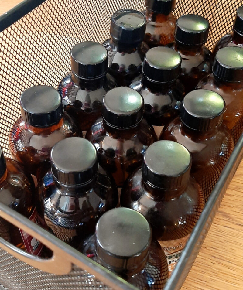 Several amber glass bottles sit in a metal mesh box, just wide enough to hold three bottles across.