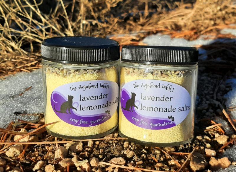 Two clear glass jars of bath salts, yellow with a layer of lavender flowers on top.