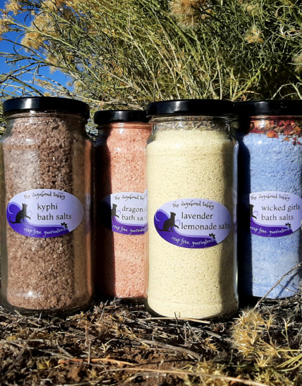 Four tall glass jars of bath salts, each a different color.