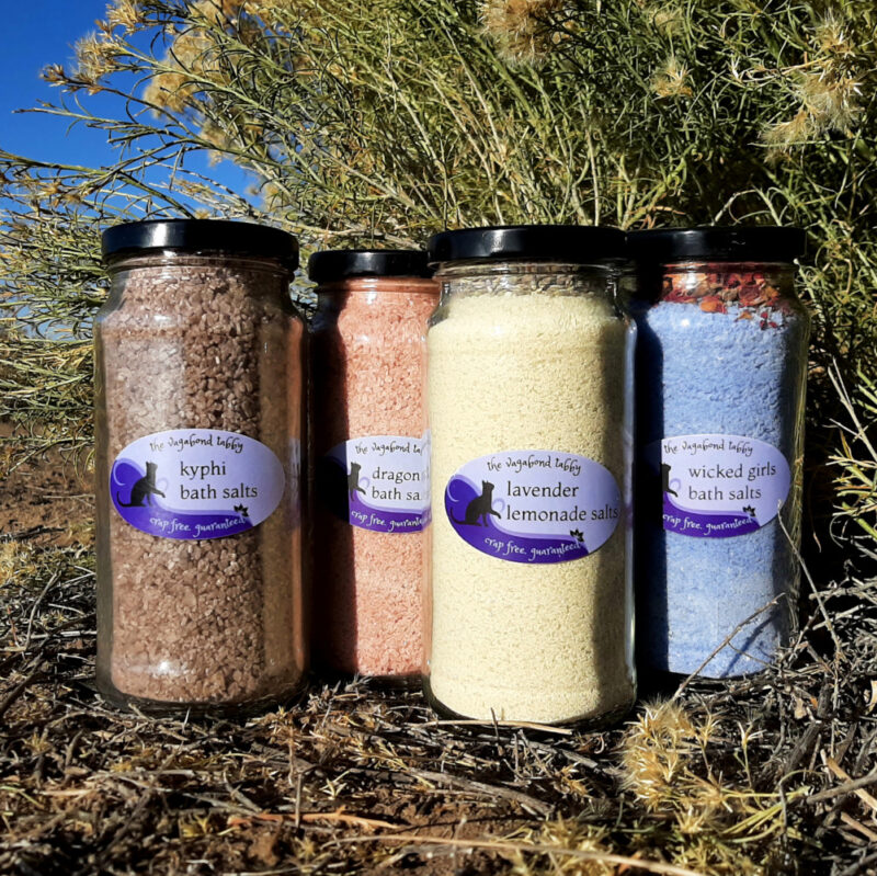 Four tall glass jars of bath salts, each a different color.