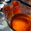 Two glass salve jars sit next to a big glass mixing bowl; all are filled with golden-orange salve.