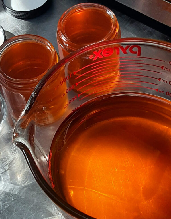 Two glass salve jars sit next to a big glass mixing bowl; all are filled with golden-orange salve.