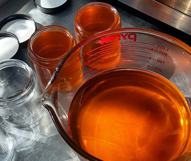 Two glass salve jars sit next to a big glass mixing bowl; all are filled with golden-orange salve.