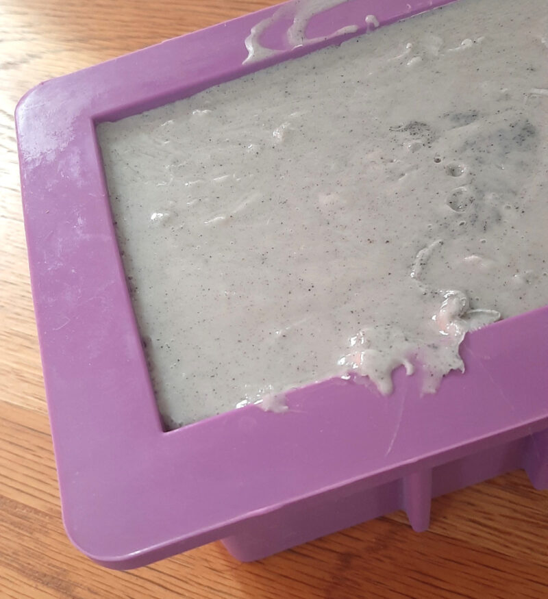 A purple soap mold holds speckled grey soap.