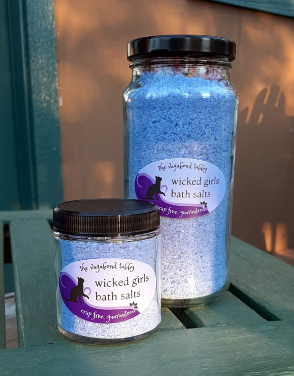 Two clear glass jars filled with blue bath salts. The very top of the taller one holds a layer of rose petals.