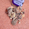 A metal tin labeled ponderosa resin sits next to a small pile of lumps of golden-brown resin.