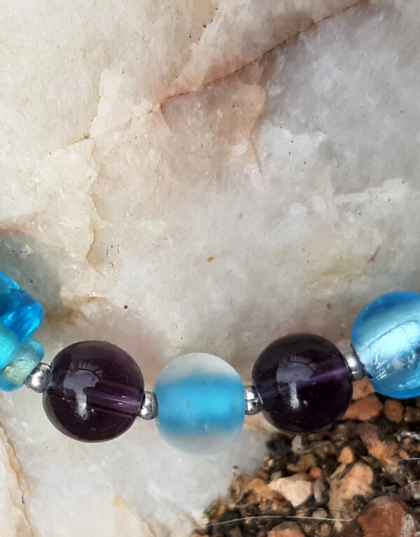 A close view of some of the beads. They alternate between teal and purple; most are spheres, but one slightly larger teal one is a cylinder. Tiny silver-colored beads separate the larger ones.