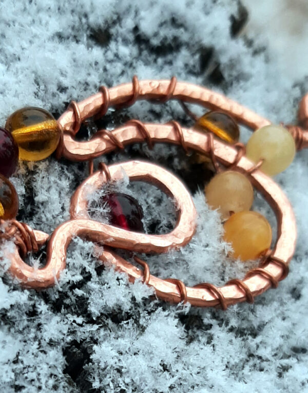 A curving, looping shape in copper wire is adorned with round glass beads ranging in color from yellow through various ambers to red.