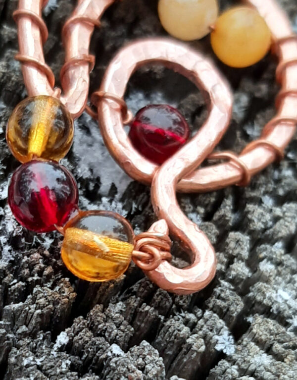 A curving, looping shape in copper wire is adorned with round glass beads ranging in color from yellow through various ambers to red.