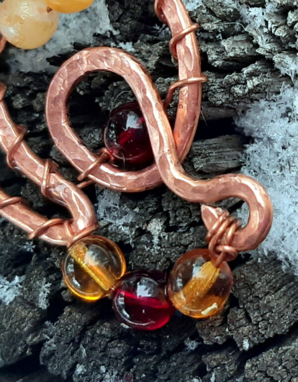 A curving, looping shape in copper wire is adorned with round glass beads ranging in color from yellow through various ambers to red.