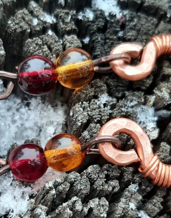 Each earring curves hammered copper down into and through a single loop with a pale yellow glass bead; two more, amber then deep red, hang below.