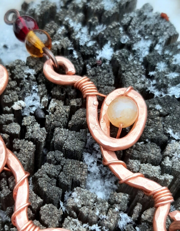 Each earring curves hammered copper down into and through a single loop with a pale yellow glass bead; two more, amber then deep red, hang below.