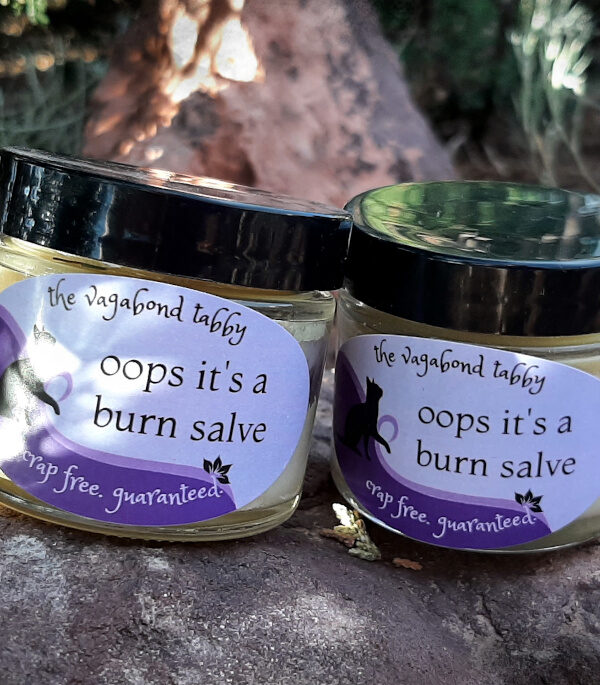 Two small clear glass jars filled with pale yellow salve. The labels say 'oops it's a burn salve'.