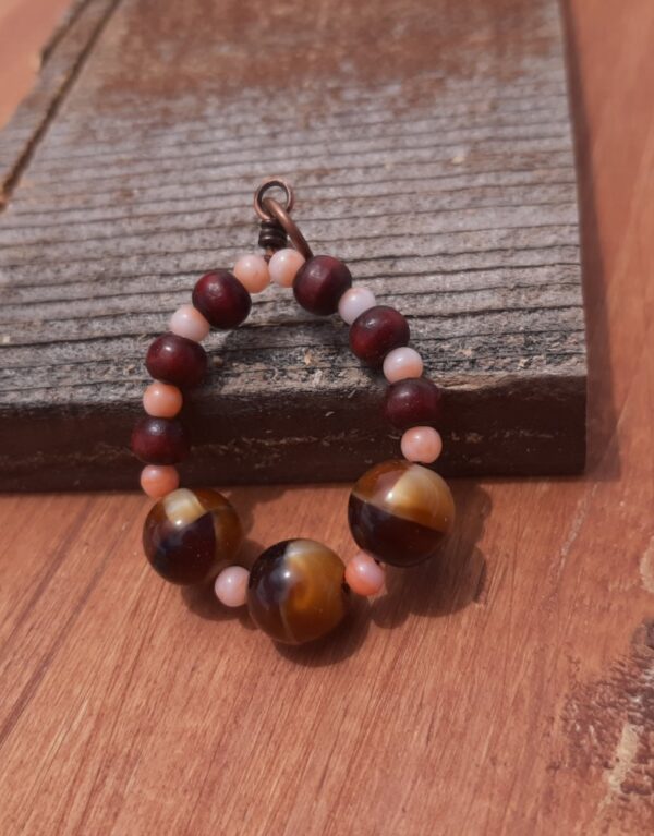 Beads, peach and reddish wood and stripey gold and brown, are threaded onto a simple loop of copper wire.