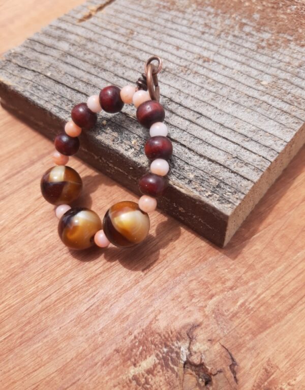 Beads, peach and reddish wood and stripey gold and brown, are threaded onto a simple loop of copper wire.