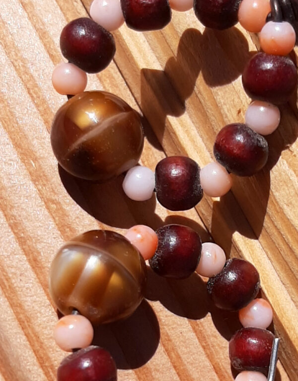 Each earring is a loop strung with alternating tiny peach beads and slightly bigger red wooden ones, with a larger stripey brown and gold bead at the bottom.