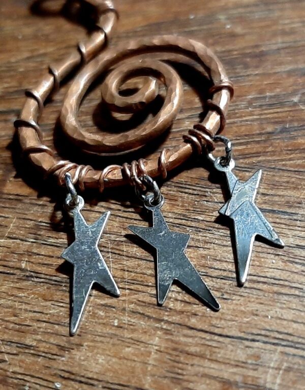 A wide spiral in hammered copper wire, with three tiny, flat, asymmetrical stars hanging from the bottom.