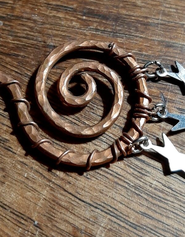 A wide spiral in hammered copper wire, with three tiny, flat, asymmetrical stars hanging from the bottom.