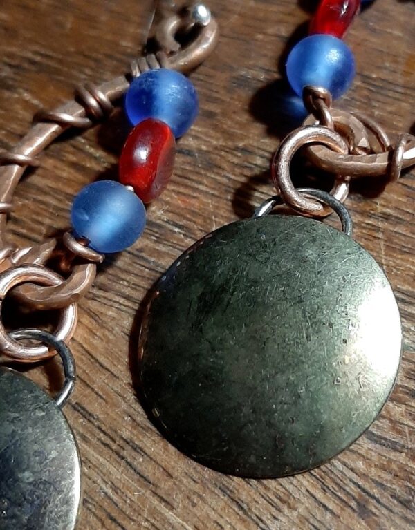 Hammered copper in a shallow c-shape, mirrored with strung beads, blue and red. Below hang domed brass circles, weathered til they resemble a moon.