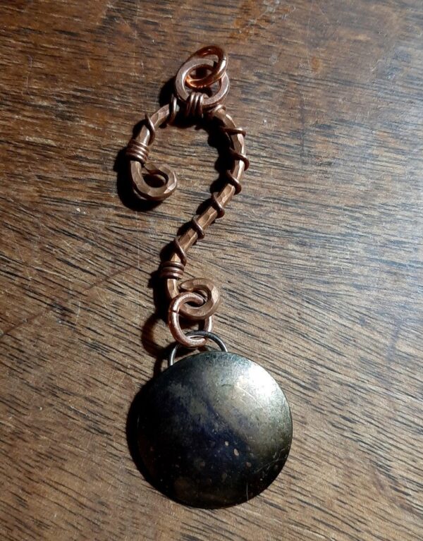 Hammered copper wire in the shape of a question mark. From the bottom hangs a domed brass circle.