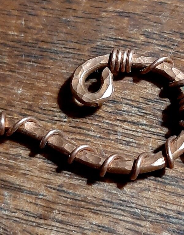 Hammered copper wire in the shape of a question mark. From the bottom hangs a domed brass circle.