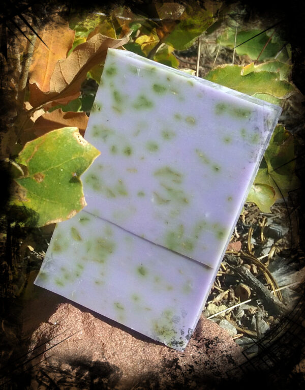 A single bar of soap, purple speckled with green herbs.