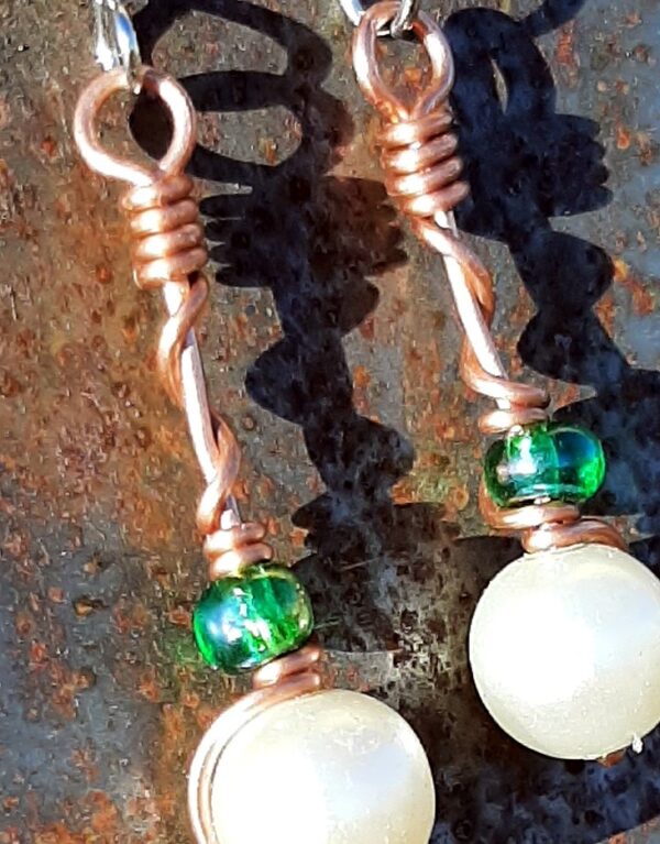 Each earring has a round white bead with an oval green glass bead above, strung on copper wire that curves back up around each bead, then twists around itself.