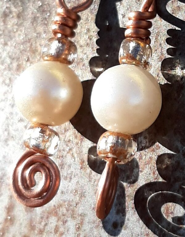 Each earring has a round white bead with a sparkly orange-brown bead to either side, all strung on copper wire that ends at the bottom in a neat spiral.