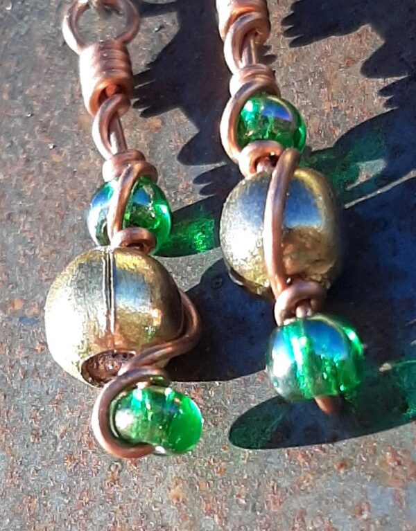 Each earring has round brass beads with oval green glass to either side, strung on copper wire that curves back up around each bead, then twists around itself.