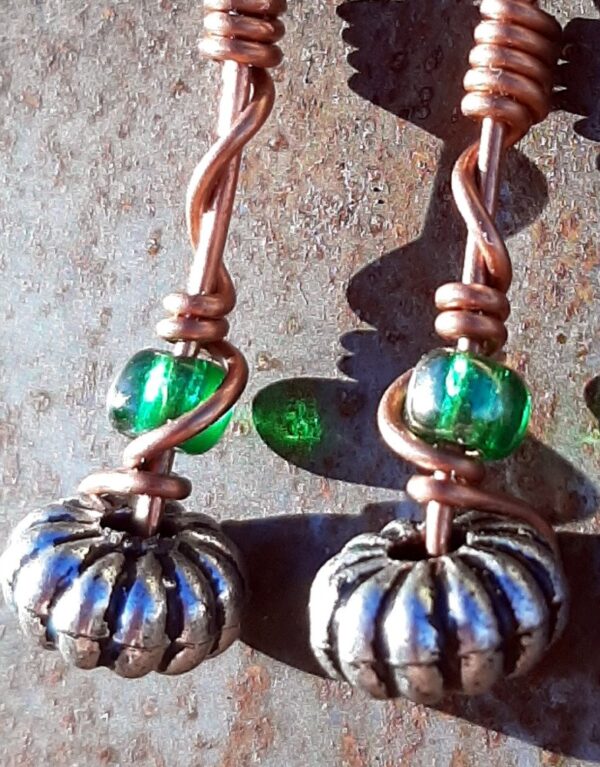 Each earring has an oval silver-colored bead with a green glass bead above, all strung on copper wire that curves back up around each bead, then twists around itself.