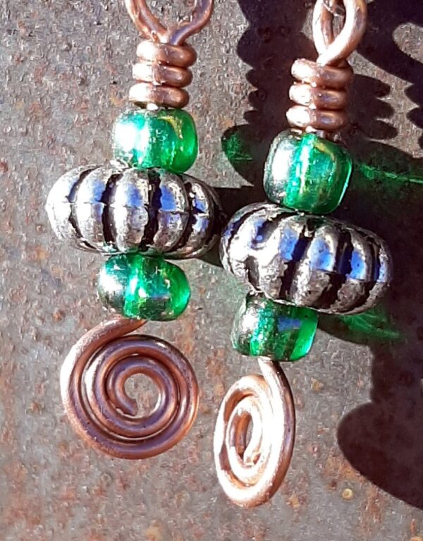 Each earring has an oval silver-colored bead with a green glass bead to either side, all strung on copper wire that ends at the bottom in a neat spiral.