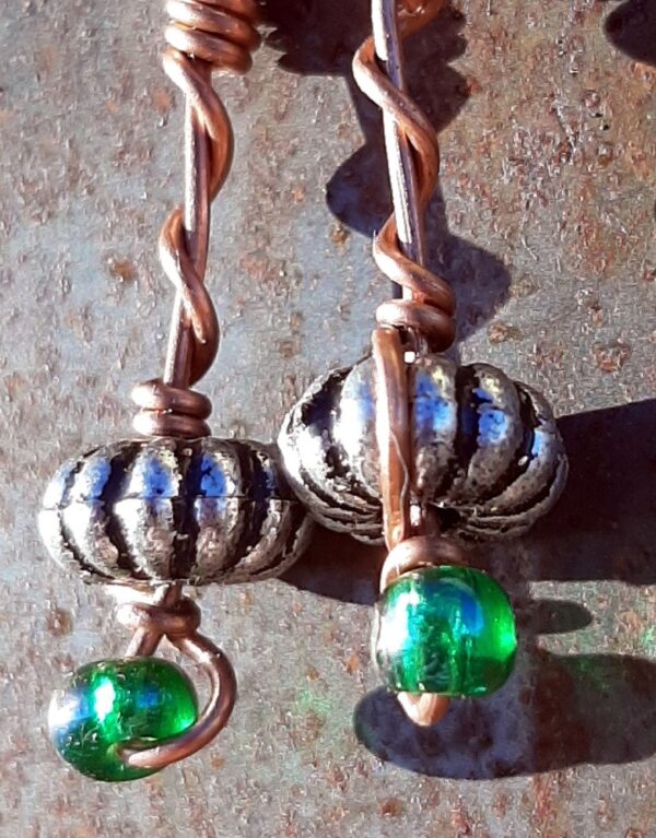 Each earring has an oval silver-colored bead with a green glass bead below, all strung on copper wire that curves back up around each bead, then twists around itself.