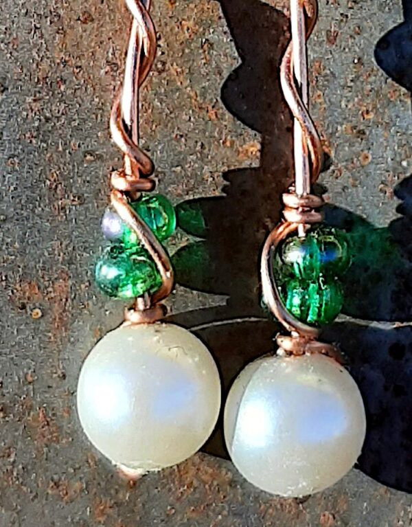 Each earring has round white beads with two oval green glass above, strung on copper wire that curves back up around each bead, then twists around itself.