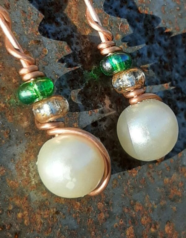 Each earring has a round white bead with a clear yellow glass bead and a green glass bead above, all strung on copper wire that curves back up around each bead, then twists around itself.