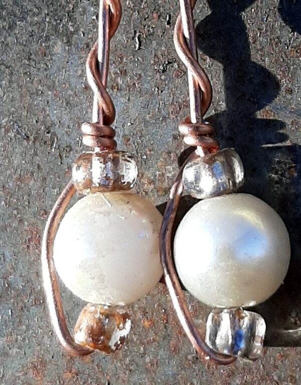 Each earring has round white beads with oval clear glass to either side, strung on copper wire that curves back up around all three beads, then twists around itself.