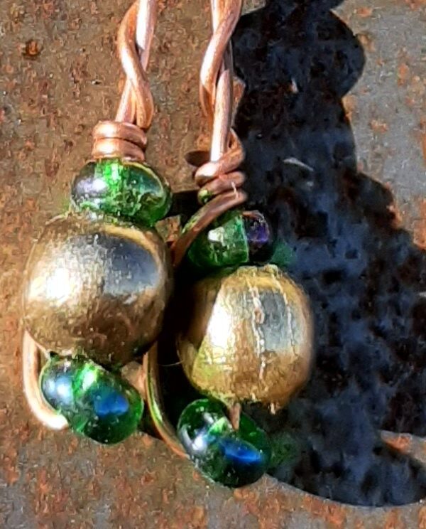 Each earring has round brass beads with oval green glass to either side, strung on copper wire that curves back up around the three beads, then twists around itself.