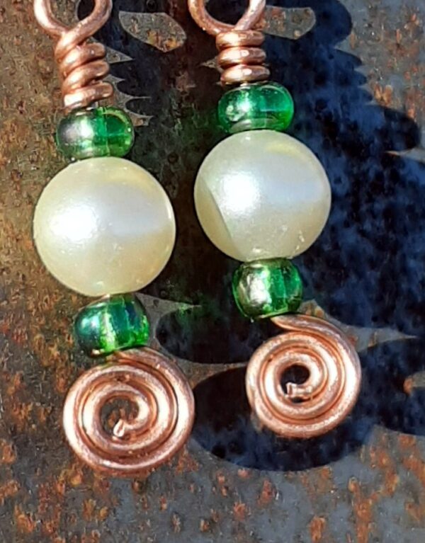 Each earring has a round white bead with a kelly green bead to either side, all strung on copper wire that ends at the bottom in a neat spiral.