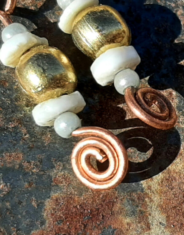 Each earring has a round brass bead with a disc-shaped bone bead above and below, and a small round pale blue bead to either side of those. All are strung on copper wire that ends at the bottom in a neat spiral.