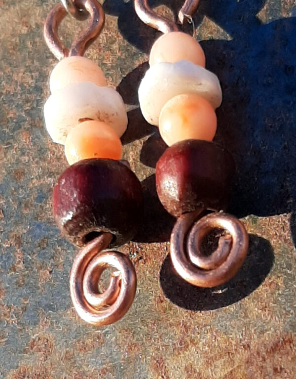 Each earring has a disc-shaped bone bead between two round peach-colored beads. below them is a round red wooden bead. All are strung on copper wire that ends at the bottom in a neat spiral.