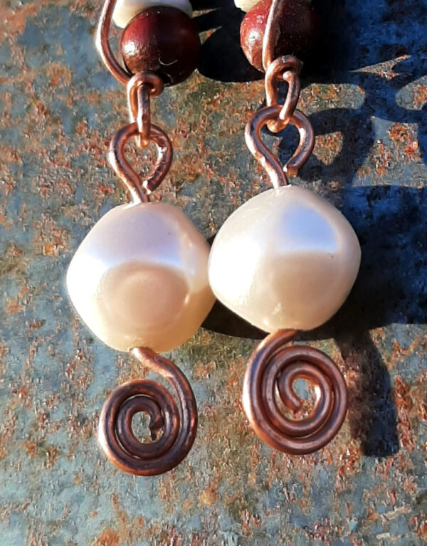 Each earring has two sections. The lower has a round white bead strung on copper wire with a neat spiral at the bottom. This is linked to a piece with a bone disc between two round red wooden beads, all strung on copper wire that curves back up around the beads, then twists around itself.