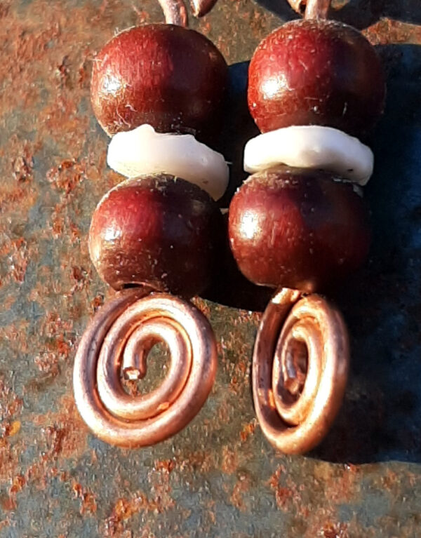 Each earring has two round red wooden beads with a disc-shaped bone bead in between. All are strung on copper wire that ends at the bottom in a neat spiral.