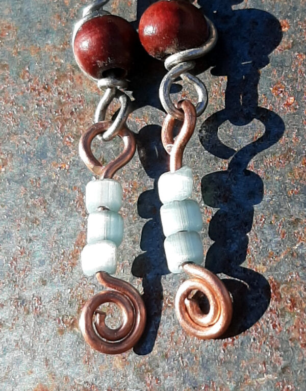 Each earring has two sections. The lower has three pale blue beads strung on copper wire with a neat spiral at the bottom. This is linked to a piece with a round red wooden bead strung on steel wire that curves back up around the bead, then twists around itself.