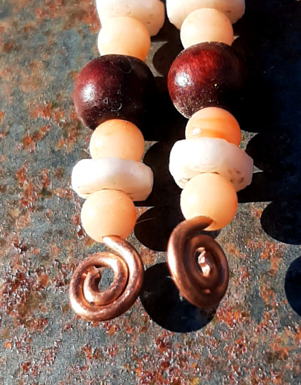 Each earring has a disc-shaped bone bead between two round peach-colored beads. below them is a round red wooden bead, and below that, another set of the peach and bone beads. All are strung on copper wire that ends at the bottom in a neat spiral.