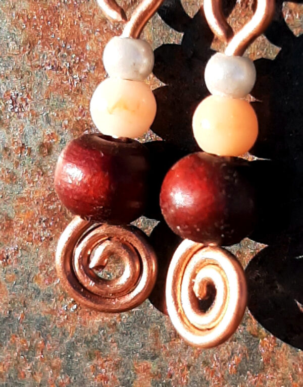 Each earring has a tiny round pale blue bead, then a slightly larger peach bead, and below those a round red wooden bead. All are strung on copper wire that ends at the bottom in a neat spiral.