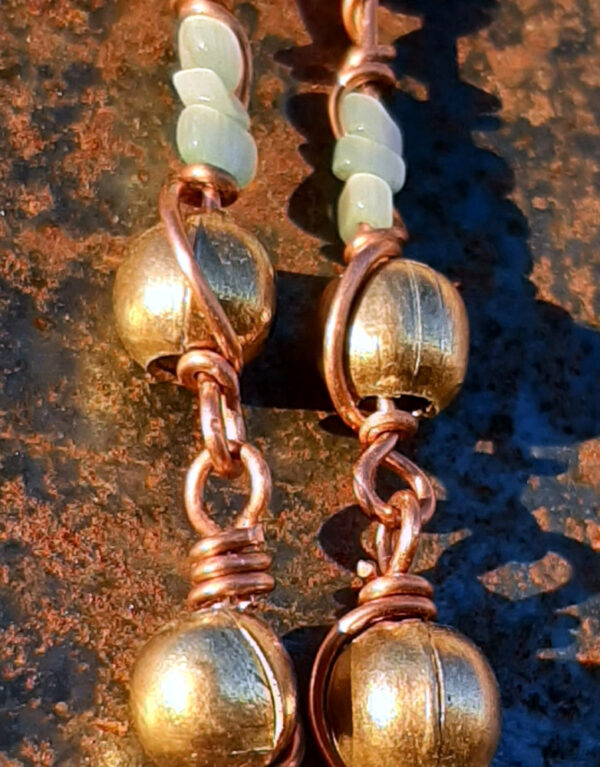 Each earring has two sections. The lower has a round brass bead strung on copper wire with a neat loop at the bottom. This is linked to a piece with another brass bead with three pale blue beads above it, all strung on copper wire that curves back up around the beads, then twists around itself.