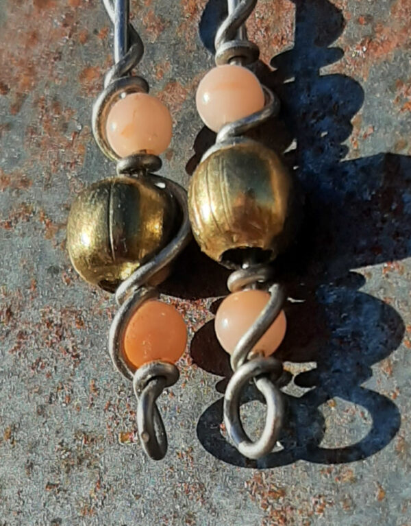 Each earring has a round brass bead with smaller peach beads above and below, all strung on steel wire that curves back up around each bead, then twists around itself.